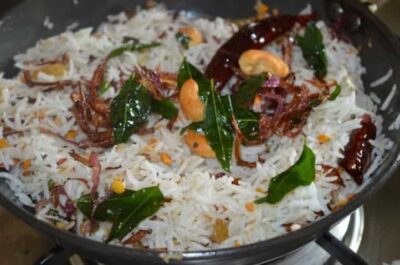 Fragrant Coconut Rice with Toasted Cashews and Curry Leaves - Plattershare - Recipes, food stories and food lovers Coconut rice garnished with toasted cashews, curry leaves, and spices, served in a black bowl.