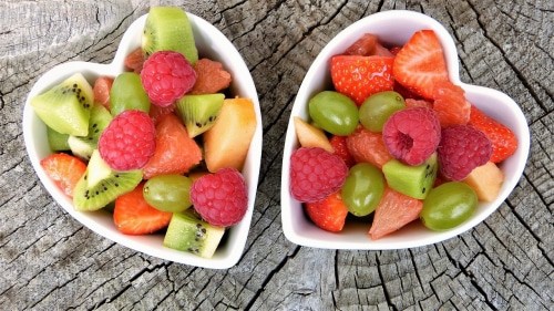 5 Super Foods For Indian Kids This Summer - Plattershare - Recipes, food stories and food lovers Fresh fruit salad in heart-shaped bowls with strawberries, kiwi, grapes, and melons on a rustic wooden surface.