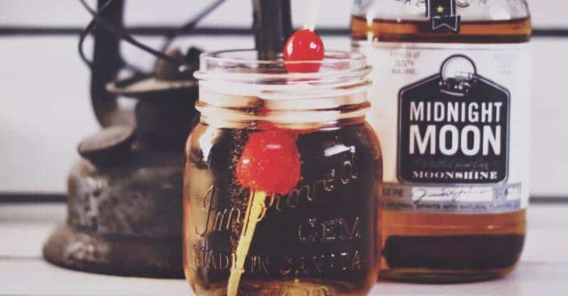 Making A Flavored Moonshine Drink - Plattershare - Recipes, food stories and food lovers Sweet cherry and cherry flavored liquor in a glass jar with a cherry on top, next to a bottle of Midnight Moon whiskey.