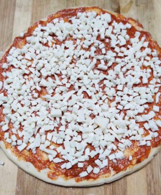 Loaded Vegetarian Pizza: A Crispy, Cheesy Delight - Plattershare - Recipes, food stories and food lovers Cheese-topped homemade pizza with tomato sauce on wooden board.