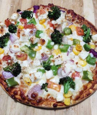 Loaded Vegetarian Pizza: A Crispy, Cheesy Delight - Plattershare - Recipes, food stories and food lovers Colorful vegetable pizza with broccoli, bell peppers, onions, and cheese on a wooden surface.