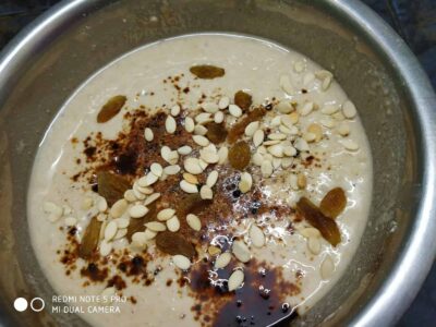 Healthy Indian Chestnut Flatbread (Naturally Sweetened) - Plattershare - Recipes, food stories and food lovers Creamy dessert with raisins, almonds, and chocolate powder in a stainless steel bowl.