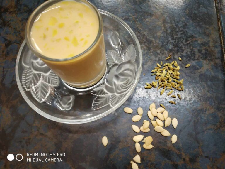 Creamy Vegan Thandai: A Refreshing & Healthy Indian Drink - Plattershare - Recipes, food stories and food lovers Sweet Indian falooda drink garnished with basil seeds and almonds in a glass on a decorative plate.