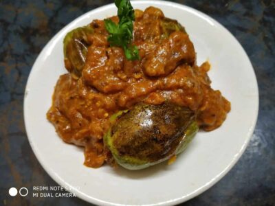 Spiced Stuffed Pointed Gourd: A Flavorful Bengali Vegetarian Recipe - Plattershare - Recipes, food stories and food lovers Spicy eggplant and tomato curry served on a white plate with fresh cilantro garnish.