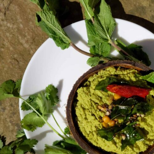 Delicious and Easy Recipes to Try This Weekend - Plattershare - Recipes, food stories and food lovers Bright green chutney in a coconut shell bowl with herbs and spices, served on a white plate outdoors.