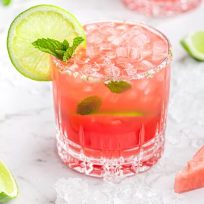 Raise a Glass Without the Buzz: Best Mocktails and Non-Alcoholic Drinks for Any Occasion - Plattershare - Recipes, food stories and food lovers Refreshing pink lemonade in a textured glass garnished with lime and mint, served over ice on a white surface.