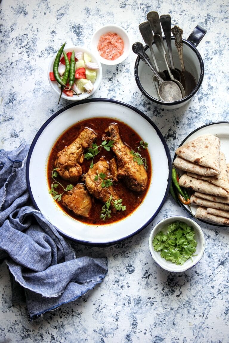 Dhaba Chicken (Rustic Chicken Curry) - Plattershare - Recipes, food stories and food lovers Spicy chicken curry served with flatbread, fresh herbs, and colorful vegetables on a rustic surface.