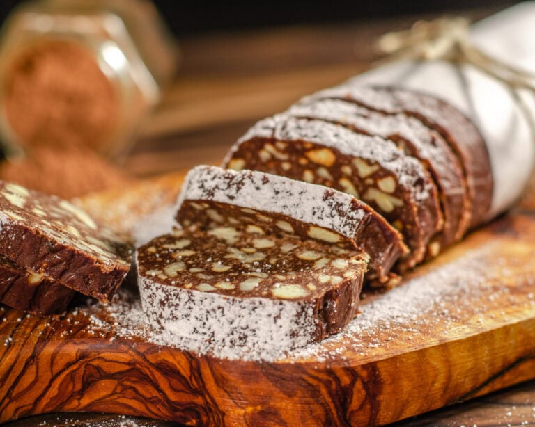 Classic No-Bake Chocolate Salami (Shokoladnaya Kolbasa) - Plattershare - Recipes, food stories and food lovers Dark chocolate salami with nuts on wooden cutting board, dusted with powdered sugar.