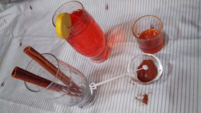 Refreshing red fruit drink garnished with lemon, served with cinnamon sticks and chocolate; perfect for summer refreshment.
