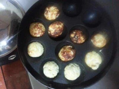 Appam cooking in a pan with golden-brown and white batter balls.