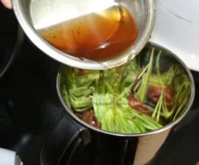 Pouring tangy broth into a pot of fresh vegetables for Wheatgrass Rasam.