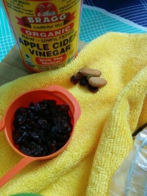 Almonds and dried cranberries with apple cider vinegar on a yellow cloth.