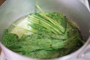 Fresh spinach being cooked for healthy spinach spaghetti with sunflower seeds.