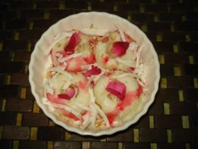 Creamy and delicious paneer kulfi served in a white bowl, garnished with rose petals and shredded co.