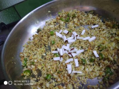 Cooked cauliflower rice with chopped onions and greens in a stainless steel pan for a delicious food recipe.