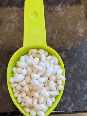 Green measuring scoop filled with puffed rice cereal, on a dark countertop.
