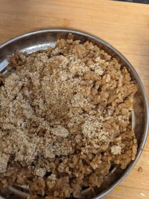 Ground meat with breadcrumbs in a stainless steel bowl on a wooden surface.