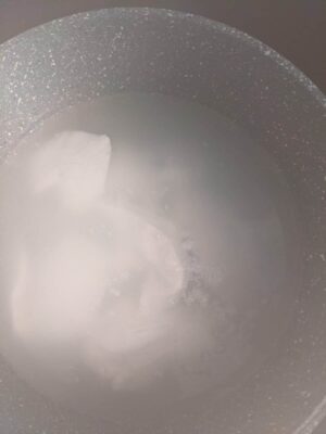 Boiling water in a stainless steel pot with a speckled finish, steam rising from the surface.