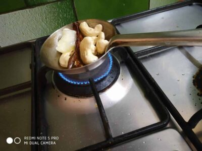 Shelled cashews and dry red chilies roasting on a stove burner.
