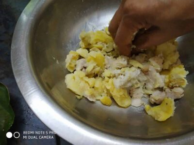 Softened boiled potatoes being mashed in a stainless steel bowl for cooking.