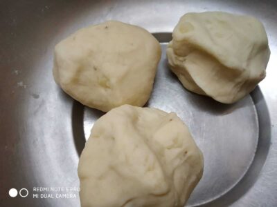 Uncooked peeled potatoes on a stainless steel plate, ready for cooking or preparation.