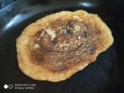 Warm crispy golden brown bread roll toasted with a sprinkling of sesame seeds on a black skillet.