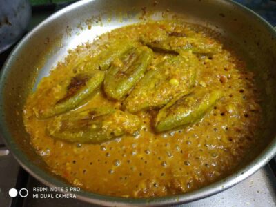 Savory eggplant curry cooking in a stainless steel pan with flavorful spices and vibrant yellow-orange sauce.