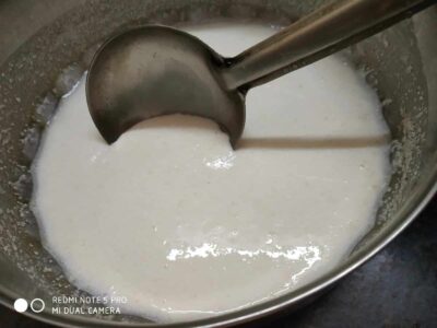 Smooth coconut milk in a stainless steel bowl with a ladle, ready for cooking or culinary use.