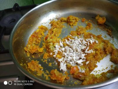 Savory pumpkin and vegetable curry with shredded coconut in a stainless steel skillet.