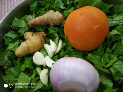 Fresh greens with garlic, ginger, tomato, and onion on a food platter.