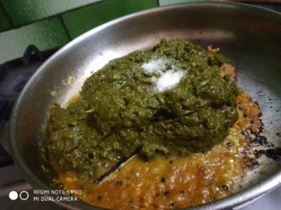 Green chutney cooking in a pan with spices and salt.