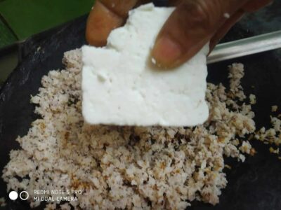 Crumbled paneer being mixed with cooked cauliflower rice for a delicious vegetarian dish.