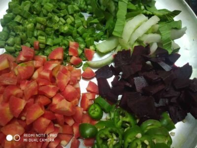Fresh chopped vegetables including tomatoes, green chilies, cucumber, and beets on a metal tray.