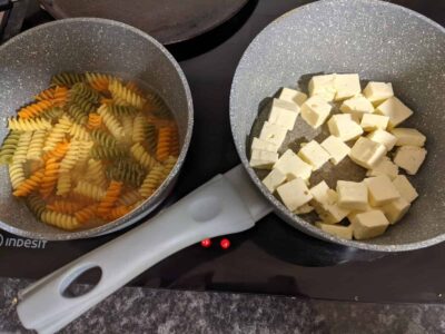 Colorful tricolor pasta boiling and cubed cheese in non-stick pans, ready for cooking.