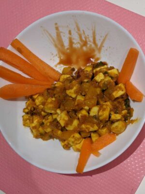 Spicy paneer curry with carrot sticks on a white plate, garnished with a drizzle of sauce.