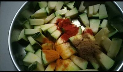 Fresh chopped cucumber with spices and turmeric in a stainless steel bowl.