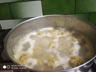 Boiling food in a metal pot with a green tiled background, showing cooking process.