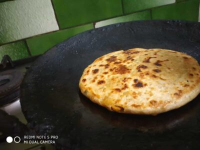 Golden brown stuffed paratha cooking on a black griddle, ready to serve delicious Indian cuisine.