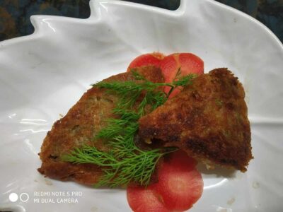 Crispy fried fish fillets garnished with fresh herbs and sliced tomatoes on a white decorative plate.