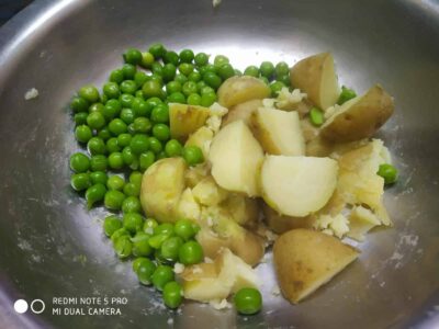 Fresh green peas and chopped potatoes in a stainless steel pan, ready for cooking.
