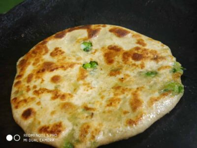 Golden toasted naan bread cooking in a skillet with green chilies.