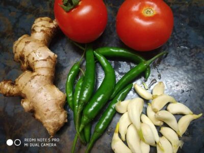 Fresh ginger, green chili, tomatoes, garlic cloves, on dark kitchen countertop for cooking.