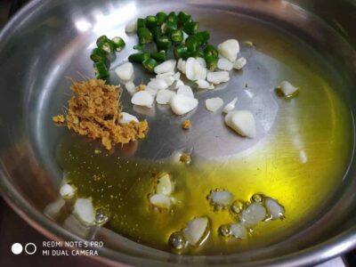 Chopped garlic, green chili, and ginger being sautéed in oil in a stainless steel pan.