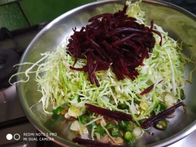 Shredded cabbage salad with beets and chopped green onions in a stainless steel bowl.