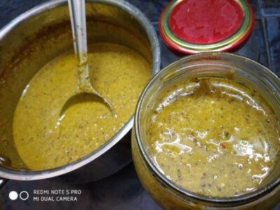 Spicy mustard seed pickle in a glass jar with a spoon, traditional Indian condiment.