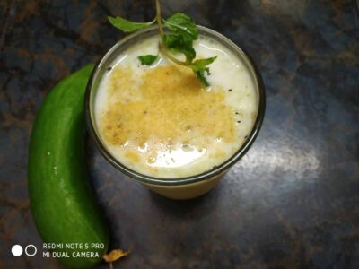 Creamy mango lassi in a glass with a mint garnish on a dark surface, alongside fresh mango.