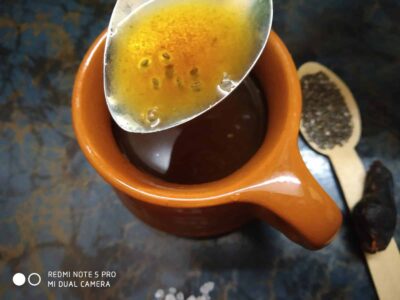 Aromatic herbal tea being prepared in an orange ceramic mug with a spoonful of herbs and honey.