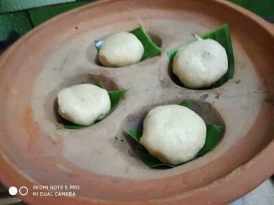 Soft Indian steamed rice flour balls resting on banana leaves in a traditional clay steamer.