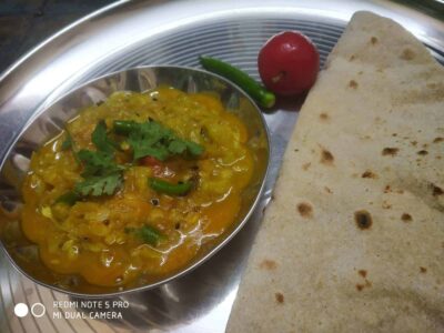 Spicy yellow lentil curry with cilantro, served with flatbread, tomato, and green chili on silver tray.