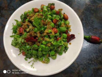 Bright green peas salad garnished with fresh cilantro and dried red chilies, served on a white plate.